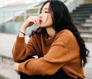 Asian woman sitting on steps looking pensive. Problems with unqualified therapists.